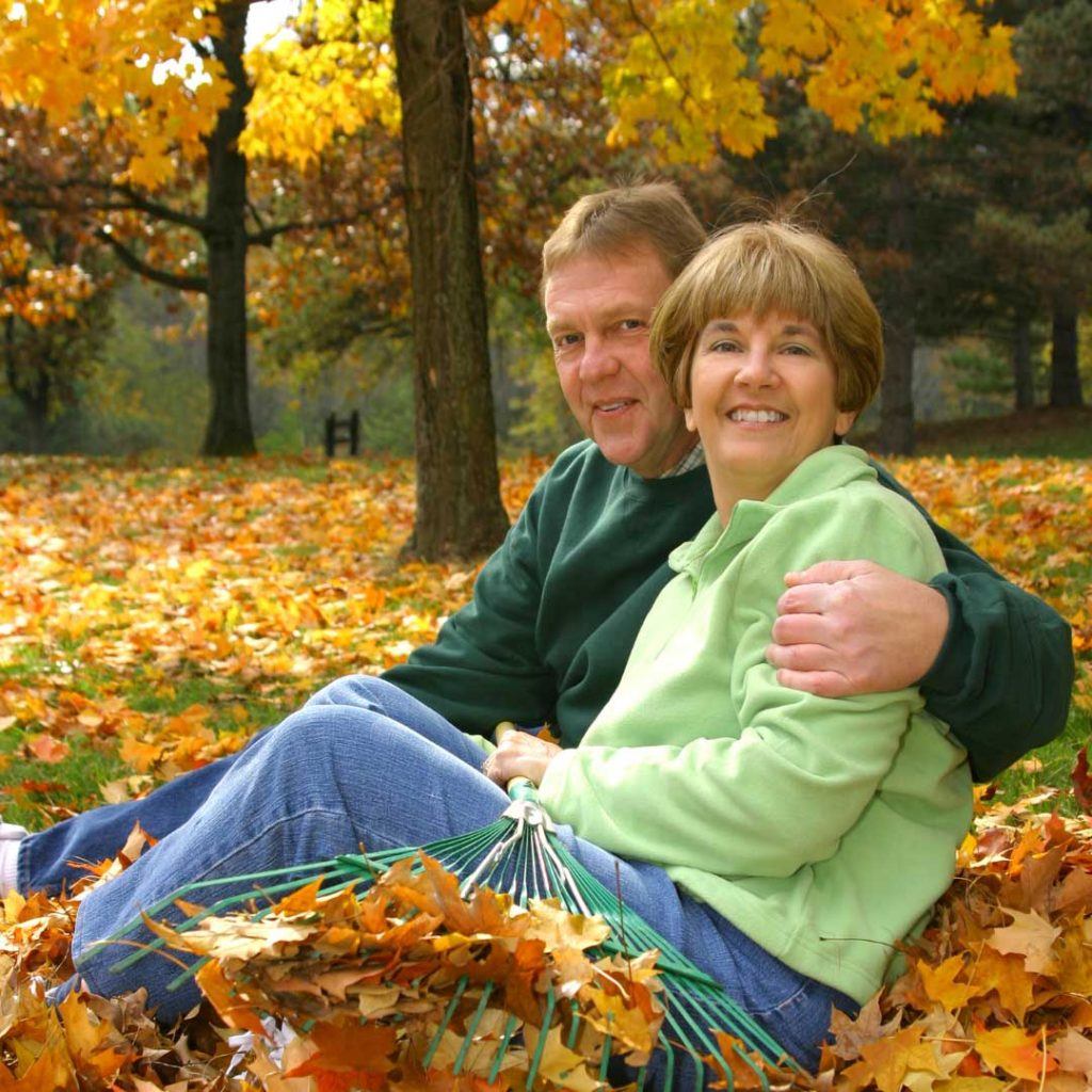 man with arm around woman sitting outside in fallen leaves
