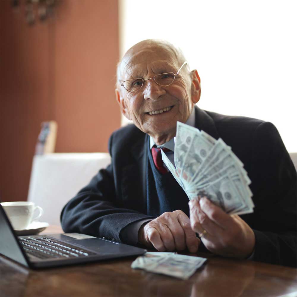 old man with glasses smiling at the camera while holding up cash