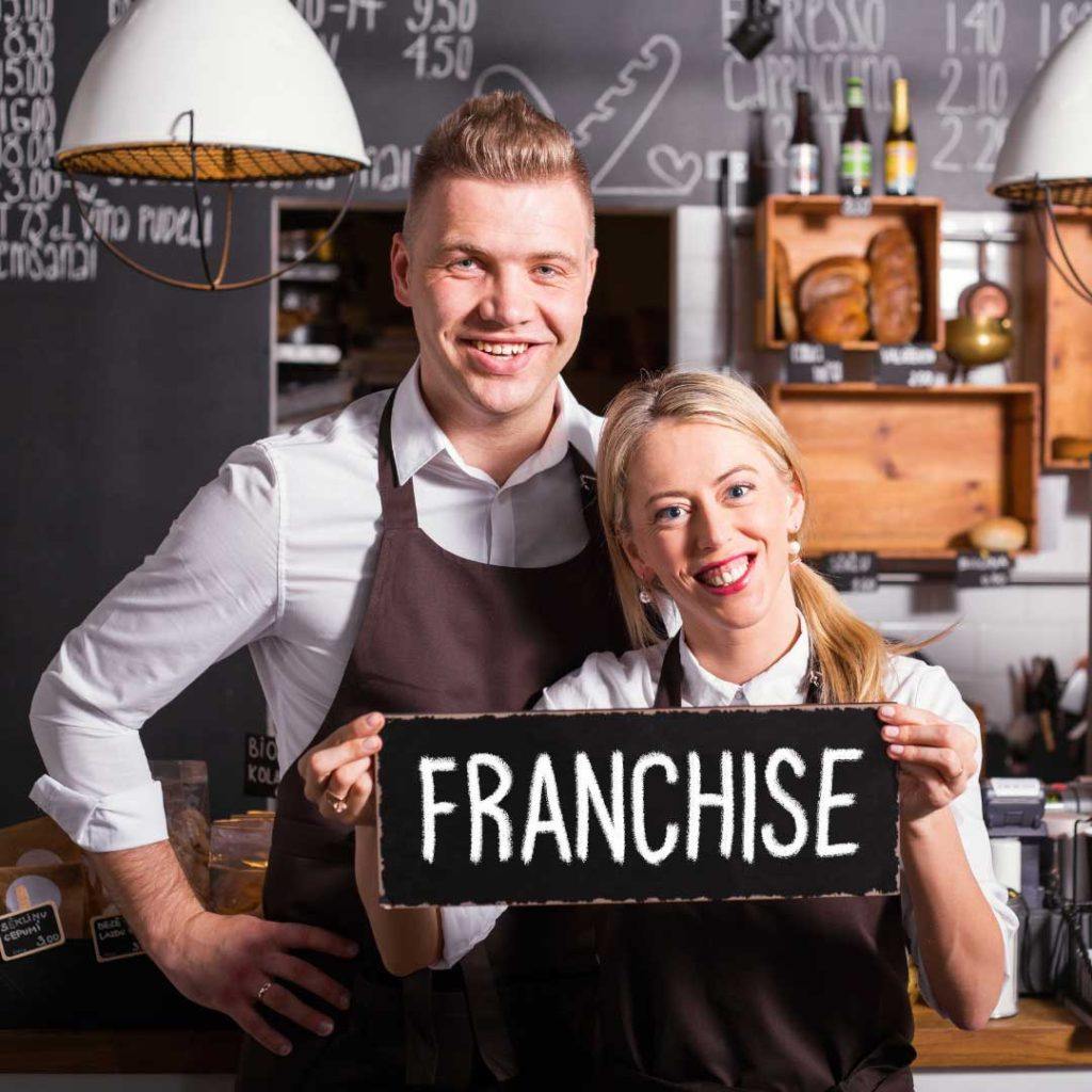 Man and woman in aprons holding a franchise sign