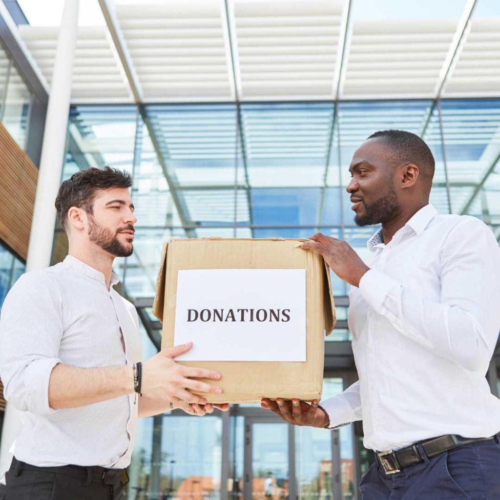 two men both wearing white polos holding a box labeled as donation