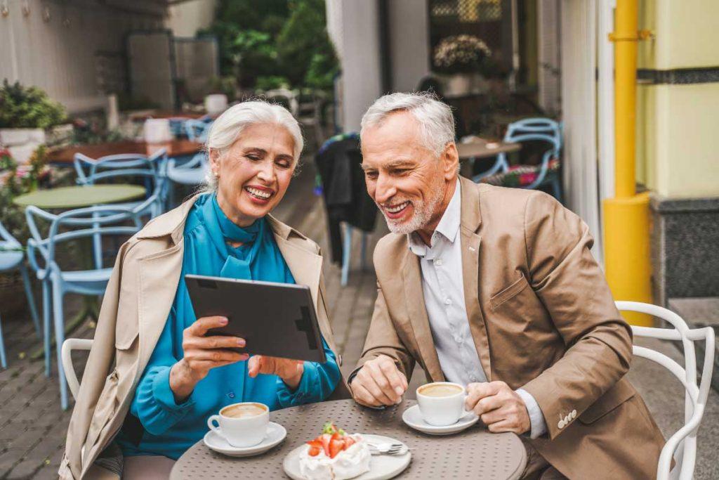 two elderly couple at a coffee table looking at a tablet