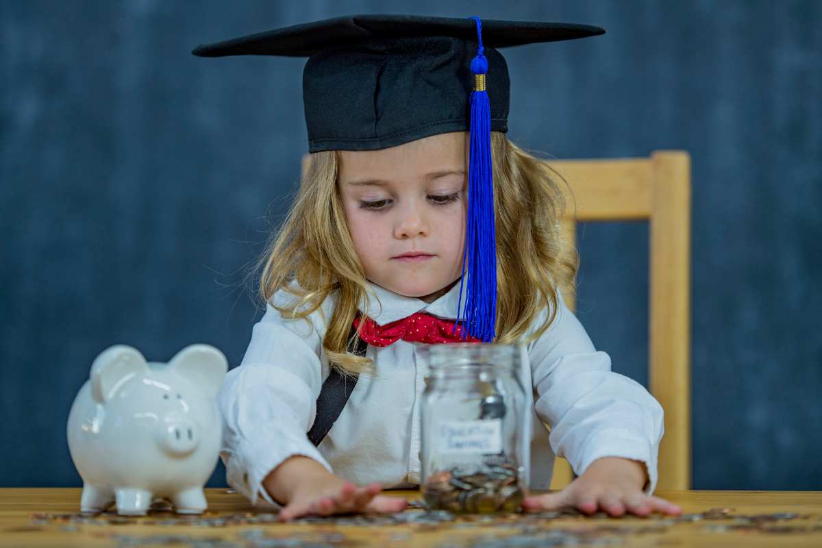 toddler wearing a mortarboard and putting coins in a jar